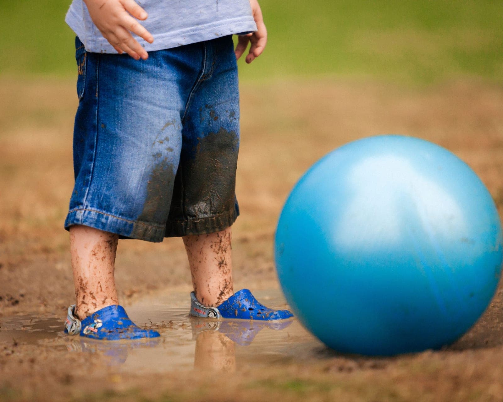 A small child's feet beside a soccer ball on grass